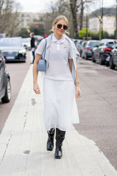Hollie Mercedes Peters wears white net polo shirt, skirt, blue bag, black boots, sunglasses outside Lacoste during the Womenswear Fall/Winter...