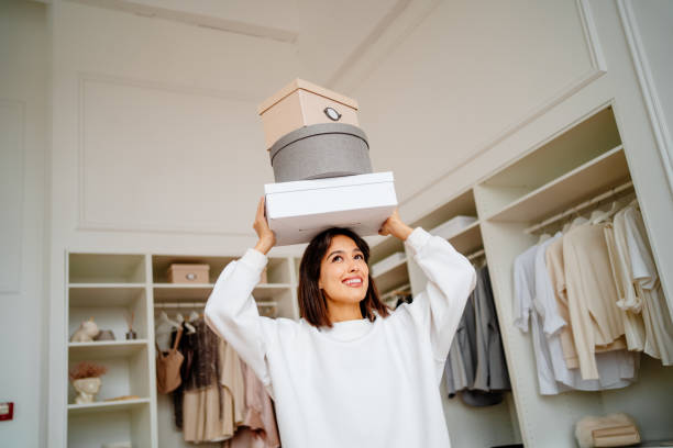 housekeeping and moving clothes boxes. smiling woman carrying clothes boxes on her head near walk in wardrobe - home decoration stock pictures, royalty-free photos & images