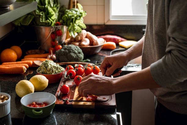 human hands slicing tomatoes over a wooden table for a vegan meal - food stock pictures, royalty-free photos & images