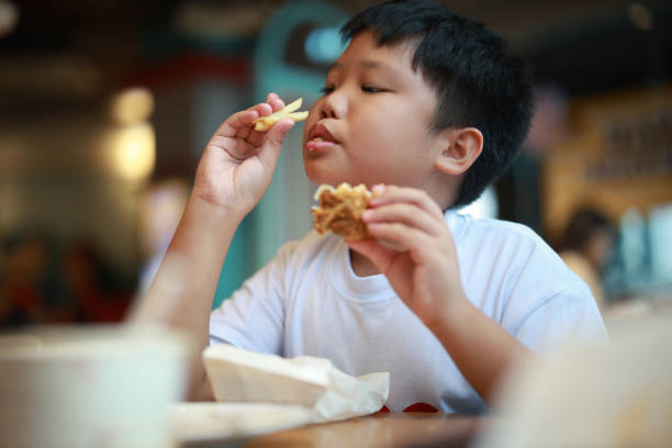 hungry boy eating burger with fries - junk food stock pictures, royalty-free photos & images