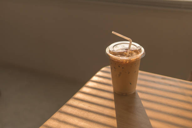 ice latte coffee in disposable cup. cold drink on wood table and sunset behind window background. - junk food stock pictures, royalty-free photos & images