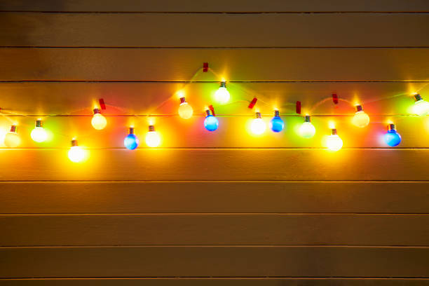 illuminated colorful string lights for party decoration at a yellow painted wooden wall in the evening - garden decoration stock pictures, royalty-free photos & images