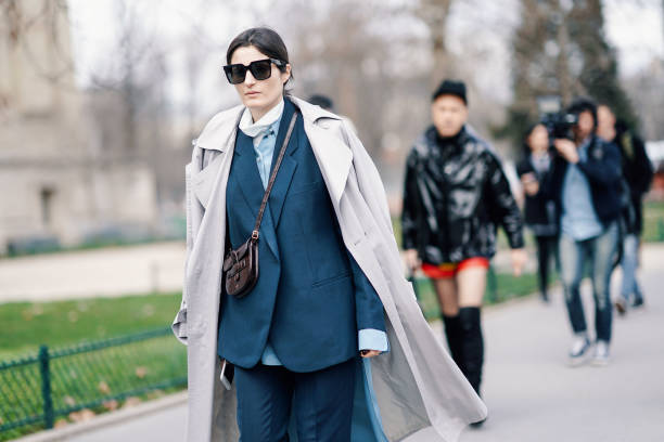 Irina Linovich wears sunglasses, a grey trench coat, a petrol-blue pantsuit, a brown alligator pattern Celine bag, outside Paco Rabanne, during Paris...