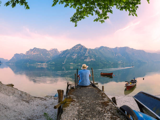 italy, lombardy, back view of man sitting on jetty at lake idro at morning twilight - travel stock pictures, royalty-free photos & images