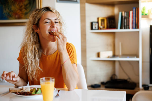 joven sonriente disfrutando del desayuno en casa - food fotografías e imágenes de stock