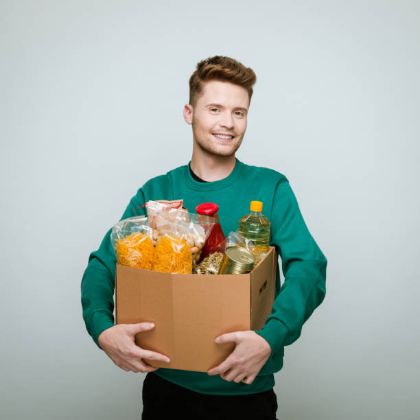 joven voluntario sosteniendo una caja de comida - food fotografías e imágenes de stock