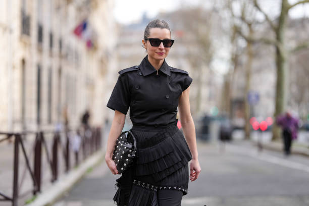 Julia Comil wears black sunglasses, a black top / jacket with ruffle details, a black leather bag with studs, outside Rokh, during the Womenswear...