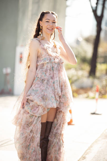 Jurga Fulti wears short in front and long in the back, light brown and pink dress and long brown leather boots outside the Chloe fashion show during...