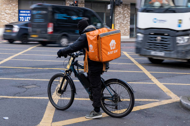 Just Eat takeaway delivery cycle courier waits at a road junction as fast moving heavy traffic passes on 3rd December 2024 in London, United Kingdom....