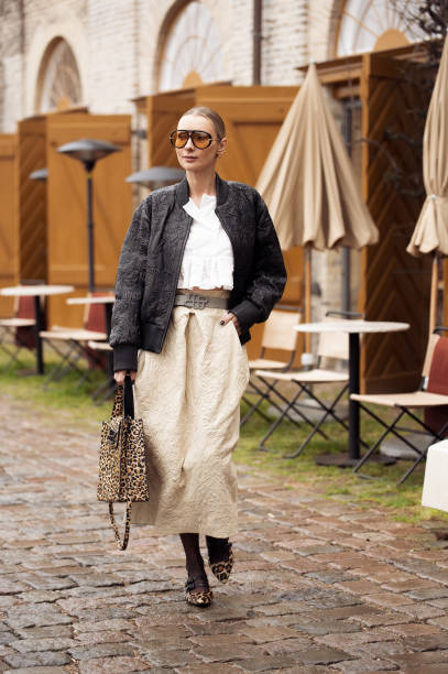 Justyna Czerniak wears beige long skirt, white crop top, black leather jacket, animal print bag, orange sunglasses and animal print shoes outside the...