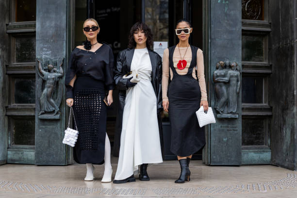 Justyna Czerniak wears black net skirt, black asymmetric top, white shoes, tights, Paco Rabanne bag & Xiayan Guo wears white dress, black blazer &...