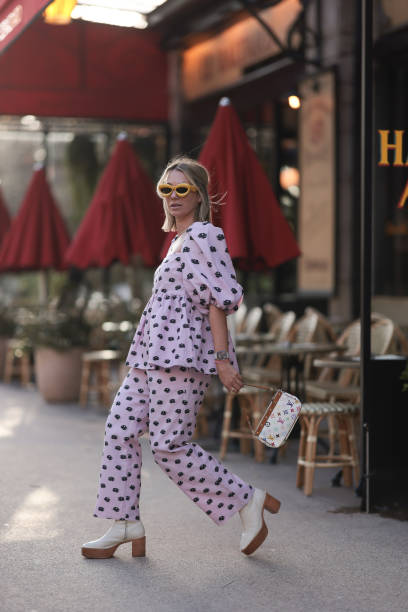 Karin Teigl seen wearing Loewe yellow sunglasses, gold necklaces, Stine Goya pink with black flower print pattern top with puffy sleeves, matching...