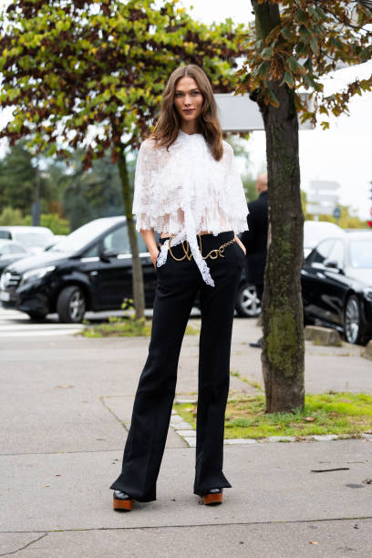 Karlie Kloss wears black and brown platform heeled mules, a Chloé gold belt, mid waist black trousers and a white see-trough lace shirt outside Chloé...