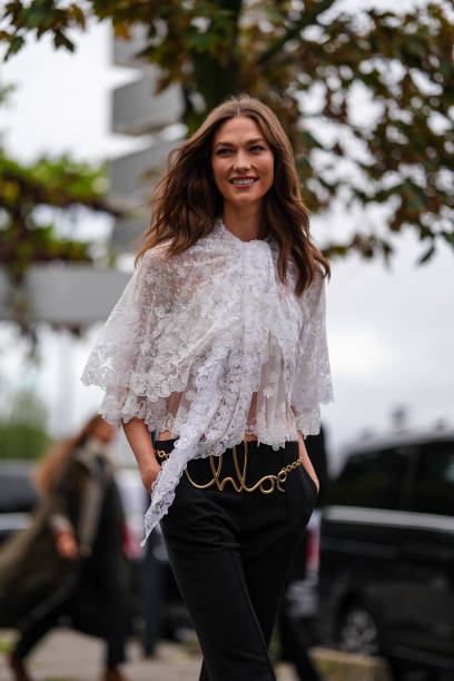 Karlie Kloss wears white sheer mesh lace flowy layered shirt, black high low-rise pants, gold Chloe belt, outside Chloe, during the Paris Fashion...