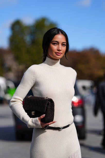 Kelsey Merritt wears white high neck long sleeve sheer mesh midi dress, black leather belt, shiny black quilted Chanel leather bag, outside Chanel,...