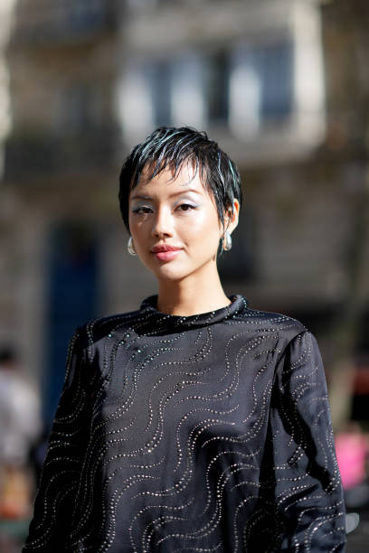Khanh Linh wears earrings, a black lustrous silk mini dress with long sleeves and printed geometric patterns, outside Stella McCartney, during the...