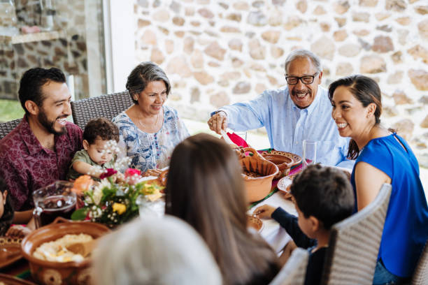 latin senior mann serviert das essen zu seiner familie am esstisch - food stock-fotos und bilder