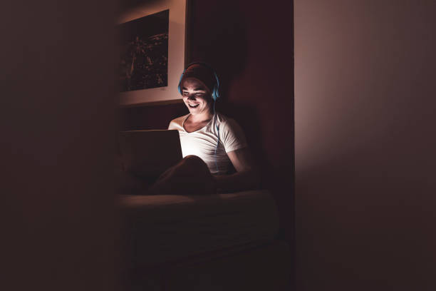 laughing man with headphones and laptop sitting on couch at home - fashion stock-fotos und bilder