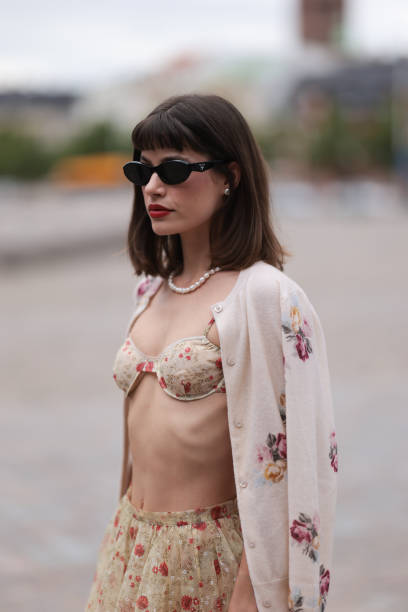 Lea Naumann is seen wearing black oval cay-eye sunglasses from Prada; small silver round earrings; a pearl necklace; a sand-beige two-piece with red...