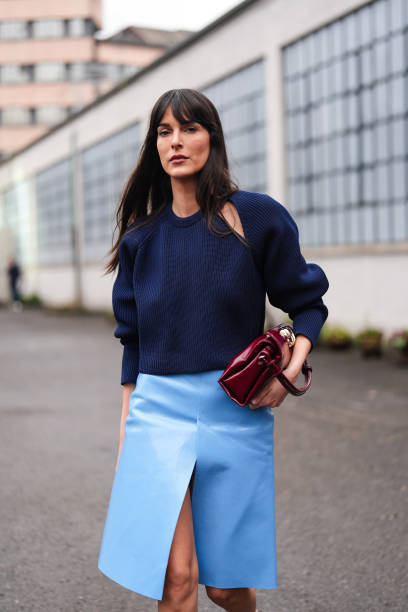 Leia Sfez wears a dark blue ribbed knitted wool pullover with puff sleeves, a burgundy leather bag, a pastel pale slit skirt in leather , pointed...