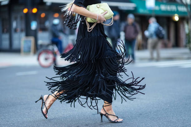 Leonie Hanne wears a neon yellow quilted leather puff bag, a black midi skirt with fringes, black high heels sandals / shoes, outside Proenza...
