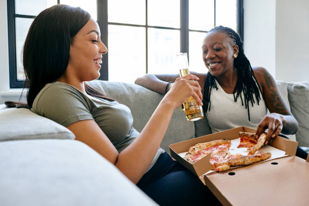 lesbian couple eating pizza at home - junk food stock pictures, royalty-free photos & images