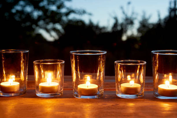 lit tea light candles in glasses in a row on table in garden during sunset - garden decoration stock pictures, royalty-free photos & images