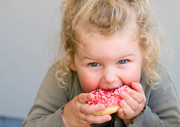 little girl eating jelly-glazed donut with sprinkles - junk food stock pictures, royalty-free photos & images