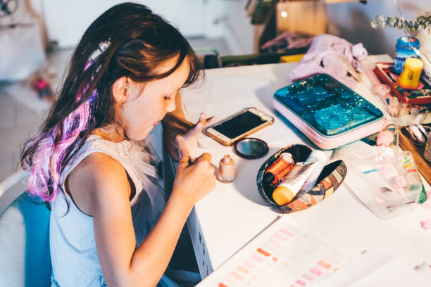 little girl paints her nails with nail polish. cute girl playing with colorful nail polish doing manicure. - nails art stock pictures, royalty-free photos & images