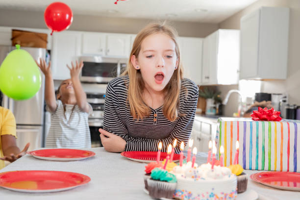 little girl prepares to blow out birthday candles on cake during party at home in kitchen - garden decoration stock pictures, royalty-free photos & images