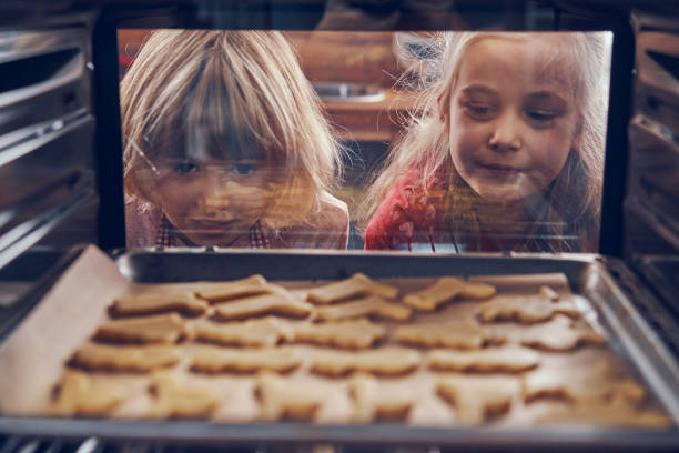 little girls waiting for christmas cookies to bake in the oven - food stock pictures, royalty-free photos & images