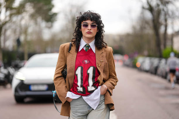 Loic Hornecker wears transparent frames black lens sunglasses, white buttoned up long sleeve shirt, dark green pattern necktie, dark red San...