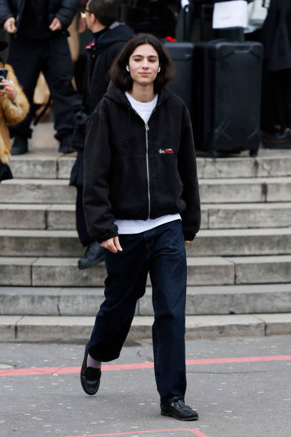 Loli Bahia wears black denim Stüssy jacket, white t-shirt, dark blue jeans, black loafaers, outside Sacai, during the Menswear Fall Winter 2025/2026...