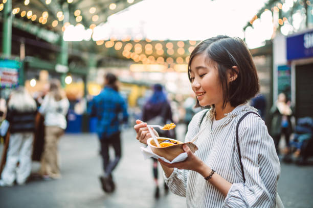 lovely cheerful girl enjoying a bowl of freshly made paella at food stall while exploring in city - junk food stock pictures, royalty-free photos & images