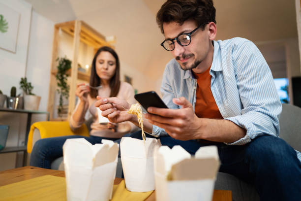 low-angle view of a young man using a phone while eating - junk food stock pictures, royalty-free photos & images