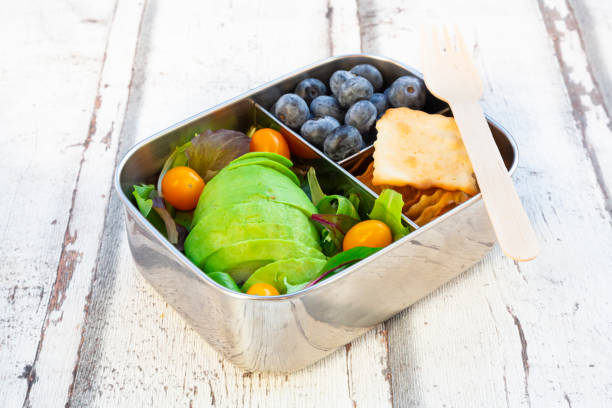 lunchbox with salad, avocado and yellow tomatoes, crackers and blueberries - junk food stock pictures, royalty-free photos & images
