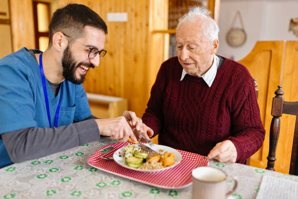 male care worker serving dinner to a senior man at his home - food stock pictures, royalty-free photos & images