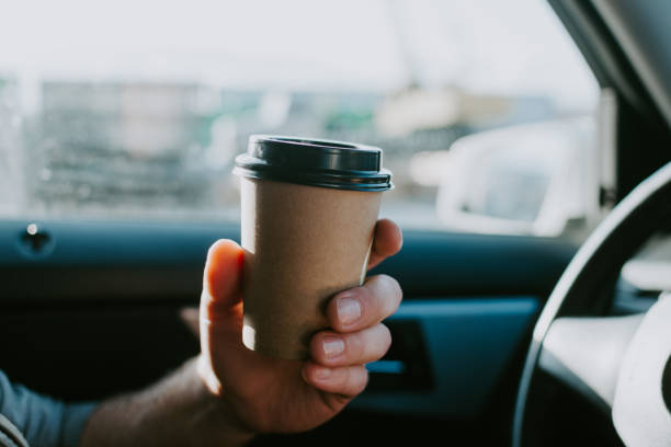 male hand with craft coffee in the car. disposable dishes, coffee on the road while driving. - junk food stock pictures, royalty-free photos & images