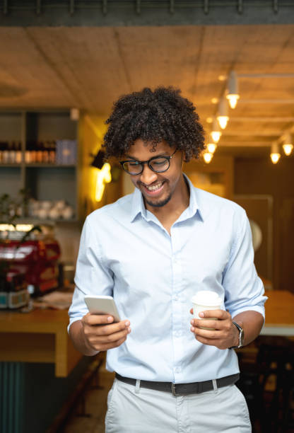 man buying a cup of coffee to go at a cafe while texting - junk food stock pictures, royalty-free photos & images