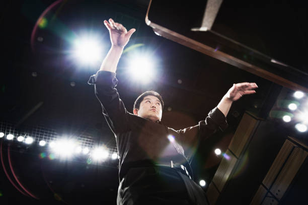 man conducting an orchestra at concert hall - concert stock pictures, royalty-free photos & images