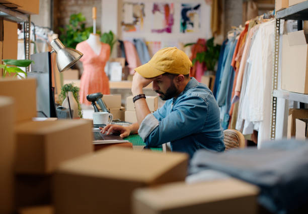man, designer and laptop stress for fashion logistics in studio with boxes for shipping, supply chain or deadline. male person, problem and boutique store for online order, distribution or package - fashion stock pictures, ro