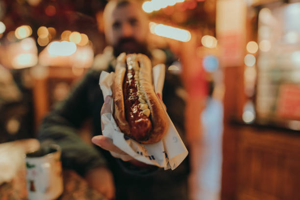 man eating a sausage hot dog and enjoying a christmas market - food stock pictures, royalty-free photos & images