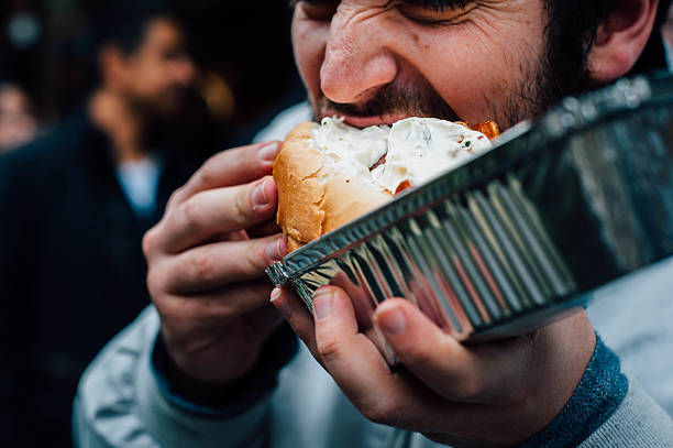 man eating hot dog on the streets - junk food stock pictures, royalty-free photos & images