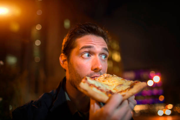 man eating pizza on city street - junk food stock pictures, royalty-free photos & images