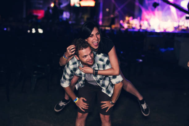 man giving piggy back to his friend in front of the stage - concert stock pictures, royalty-free photos & images