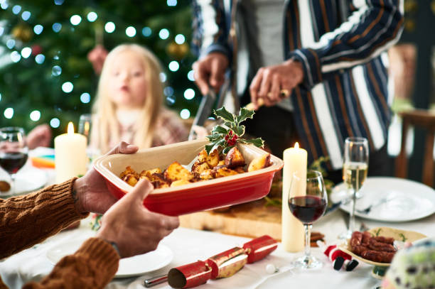 man holding serving dish with roast potatoes and a sprig of holly for christmas dinner - food stock pictures, royalty-free photos & images
