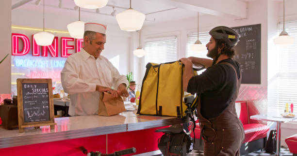 man in a white button down shirt packs order for delivery person in a 1950s styled diner - junk food stock pictures, royalty-free photos & images