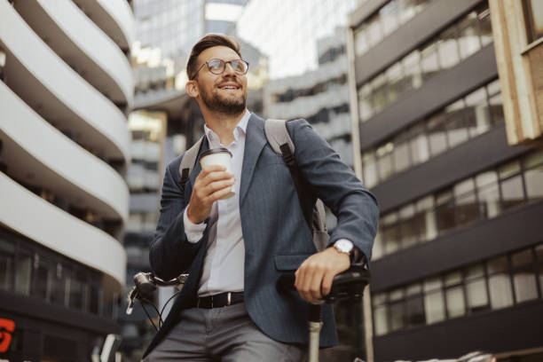 man leaning on bicycle and holding cup of coffee on the city streets - junk food stock pictures, royalty-free photos & images