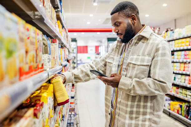 man looking at smartphone while choosing items in supermarket - food stock pictures, royalty-free photos & images