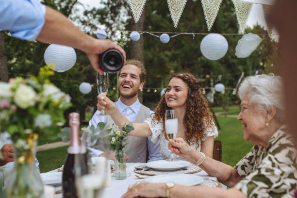 man pouring champagne into glasses for a toast at garden party. - garden decoration stock pictures, royalty-free photos & images